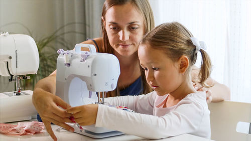 Mother teaching sewing to daughter at home