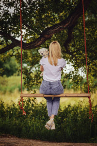 Young woman with a white dog on a tree swing.