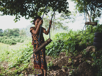 Girl standing by rope swing on field