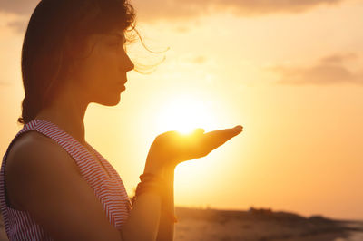 Side view of young woman against orange sky