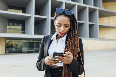 Young businesswoman with mobile phone standing outside office building