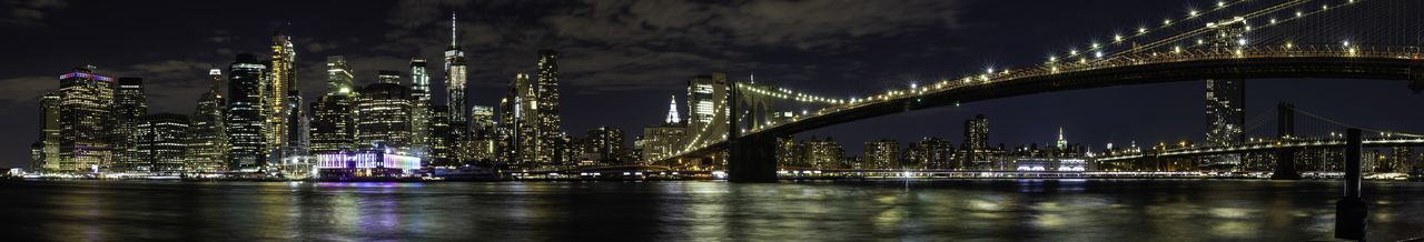 Illuminated bridge over river by buildings against sky at night