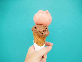 Hand holding ice cream cone against blue background