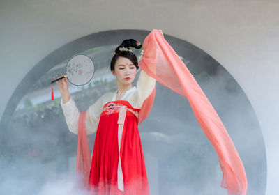 Young woman with red umbrella standing against the wall