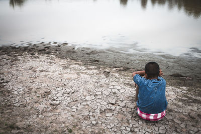 Rear view of boy sitting on land by lake