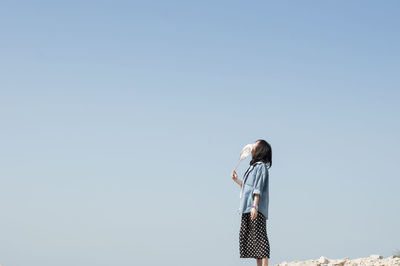 Woman holding folding fan looking up while standing against clear sky