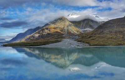 Scenic view of lake by mountains against cloudy sky