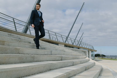 Businessman walking on staircase against sky
