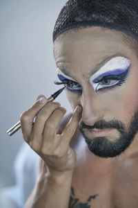 Shirtless man applying eyeliner at home