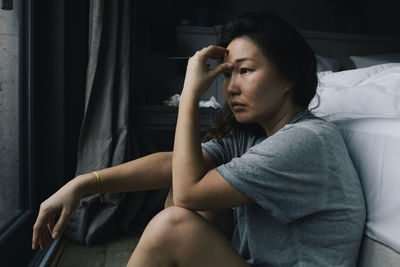 Side view of stressed woman contemplating against bed at home