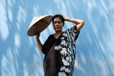 Mature woman holding asian style conical hat against wall