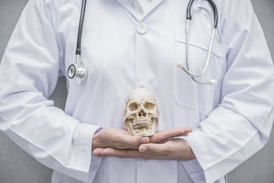 Midsection of doctor holding human skull in hospital
