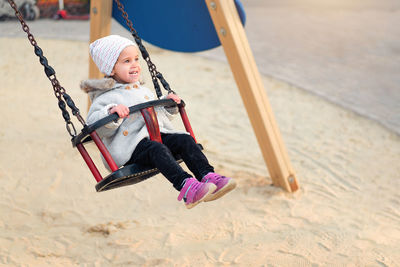 Smiling girl looking away while sitting on swing at playground