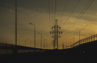Low angle view of silhouette electricity pylons against sky during sunset