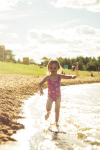 Full length of cute girl with arms raised against sky