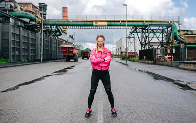 Sporty woman looking camera posing in the middle of the road in front of a factory