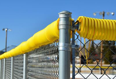 Close-up of yellow tubing on fence at softball field 