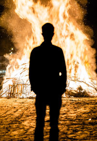 Rear view of silhouette man standing by bonfire at night