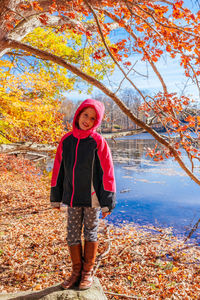 Portrait of girl wearing hooded jacket at lakeshore in forest during autumn