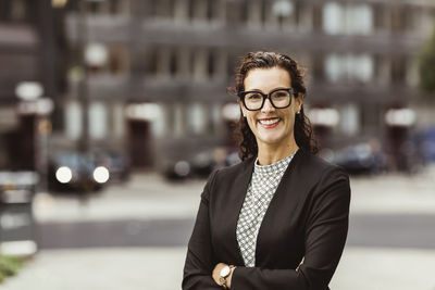 Portrait of smiling businesswoman with arms crossed standing outdoors