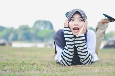 Young woman looking away while lying on grassy field