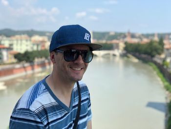 Portrait of man smiling while wearing sunglasses against river in city