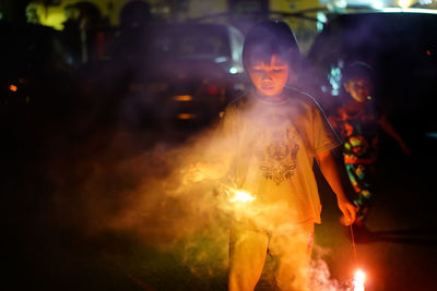 Boy holding illuminated firework at night