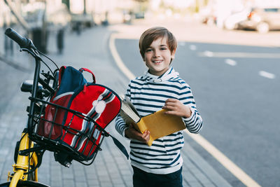 A cheerful boy holds a book in his hands and stands next to a bicycle 