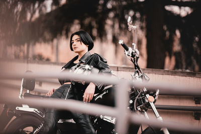 Young motorcyclist woman looking away standing by bike