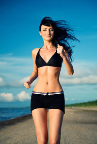 Portrait of young woman standing at beach against sky