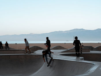 People on skateboard by sea against clear sky