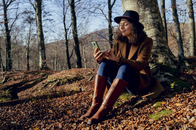 Full length of young woman sitting on land in forest