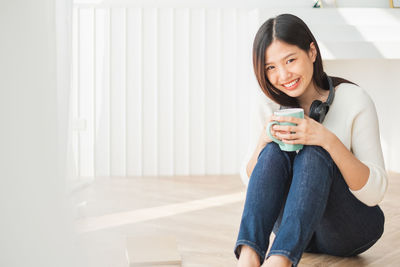 Portrait of a smiling young woman holding drink while sitting at home