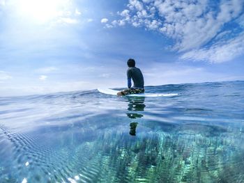 Full length of man sitting on paddleboard in sea against sky