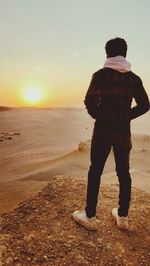 Rear view of man standing at beach against sky during sunset