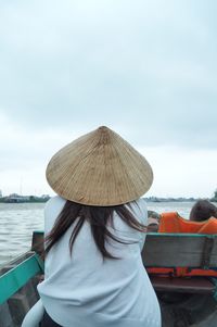 Rear view of woman sitting in boat on sea against cloudy sky
