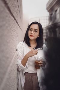 Portrait of young woman standing against wall