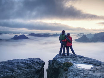 Lovely heterosexual couple looking at far sunrise in heavy clouds. dark night in foggy mountain ends