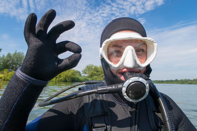 Close-up portrait of scuba diver showing ok sign against river