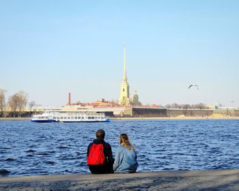 Rear view of friends on water against clear sky