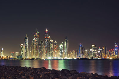 Night view of illuminated skyscrapers at dubai marina, water surface and rocks