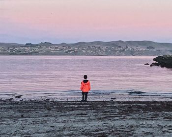 Rear view of man standing on beach against sky during sunset