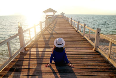 Young woman in white hat sitting on the wooden pier