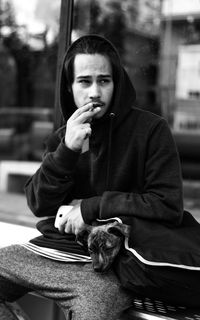 Young man smoking cigarette while sitting with puppy on bench