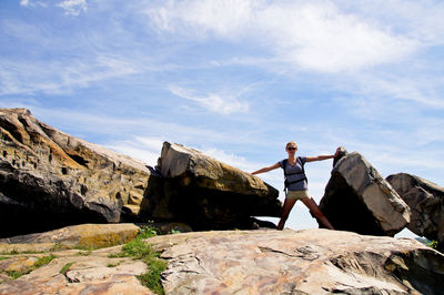 Low angle view of woman standing on rock against sky