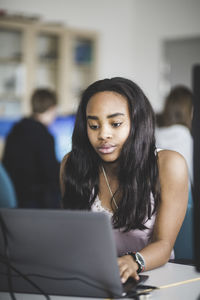 Confident female high school student using laptop at desk in classroom