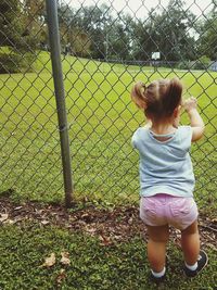 Rear view of girl standing against chainlink fence