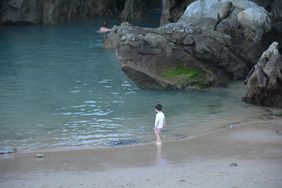 High angle view of boy standing on shore by rock formations