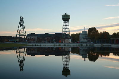 Reflection of water tower on calm lake against sky during sunset