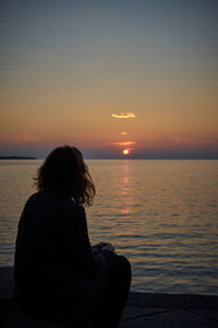 Rear view of woman looking at sea during sunset